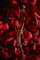 A clear borosilicate glass wand lying on a bed of red rose petals. The glass wand has a bulbous end and textured ridges along its length.